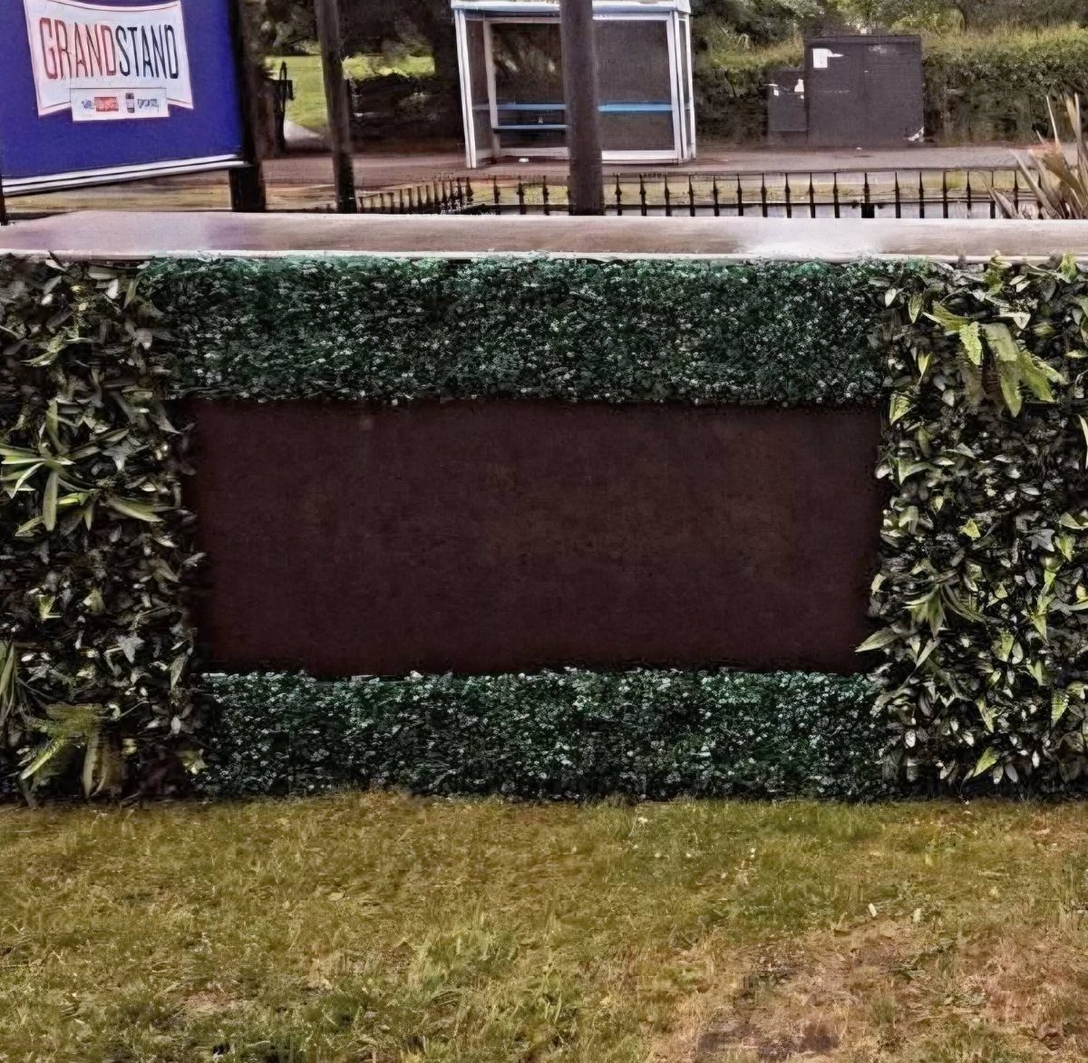 Outdoor bar counter with green hedge facade and brown panel on grass lawn