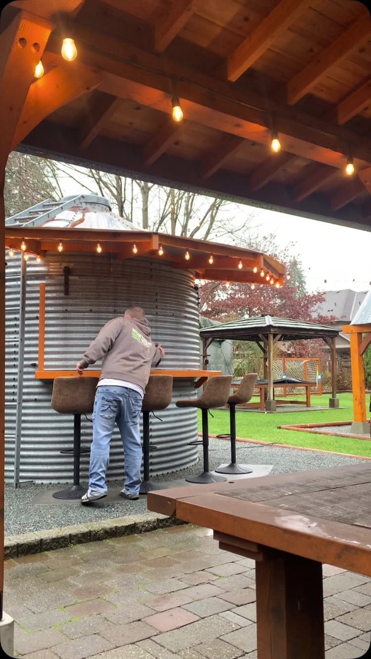 Man standing at a wooden bar attached to a corrugated metal silo outdoors