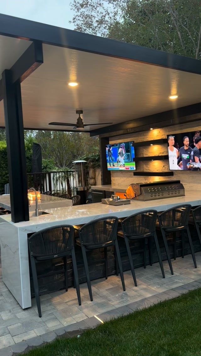 Outdoor kitchen bar with white marble countertop, built-in grill, and black bar stools.