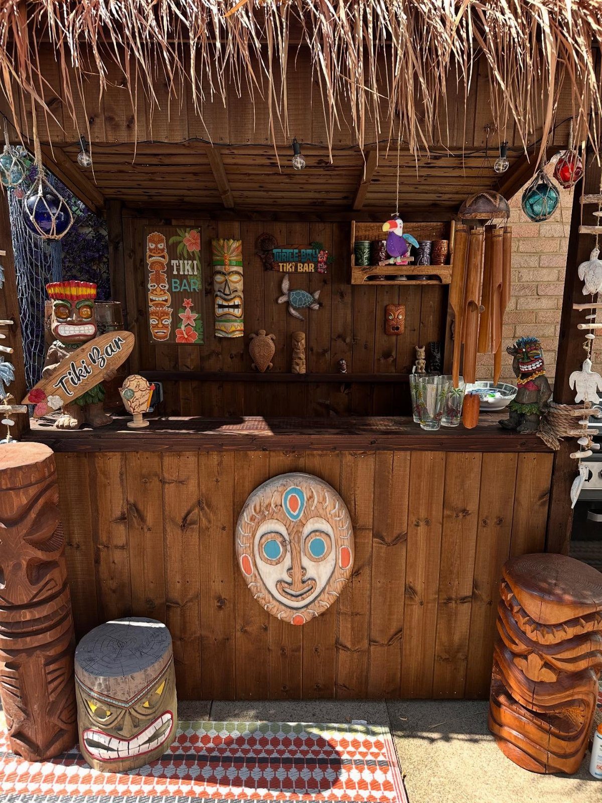 Tropical tiki bar with thatched roof, wooden counter, and carved tiki masks.