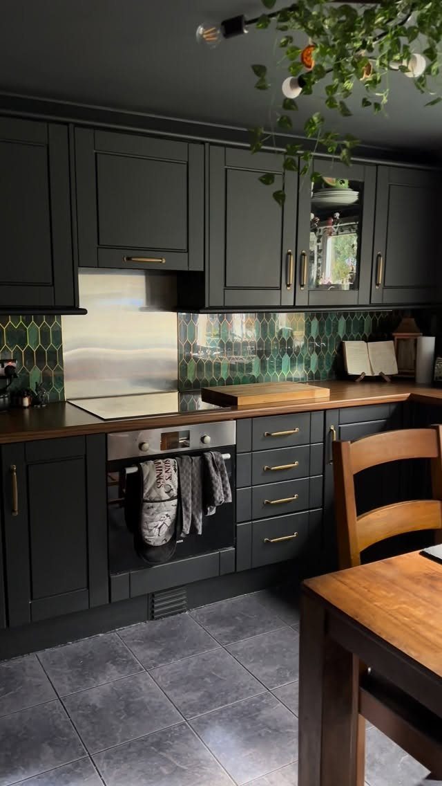 Dark charcoal kitchen cabinets with a green hexagonal tile backsplash and wooden countertops.