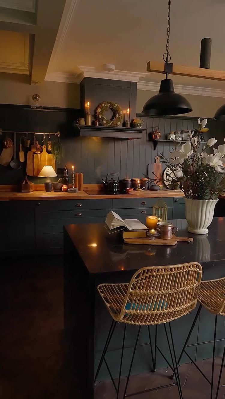 Dark green kitchen cabinets and black island with wicker stools and warm lighting