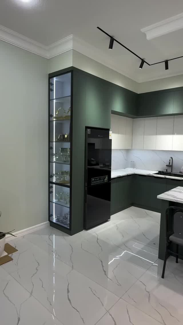 Modern kitchen with dark green cabinets, black refrigerator, and white marble flooring.