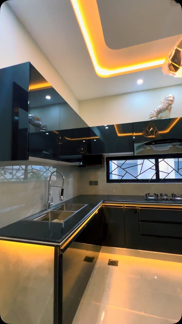 Dark green glossy kitchen cabinets with black countertops and yellow ceiling lighting.