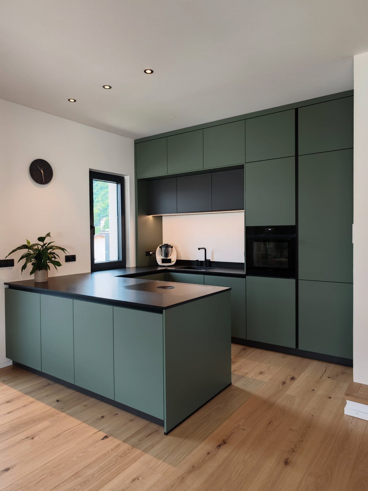 Modern kitchen with dark green cabinets, black countertops, and light wood floors.