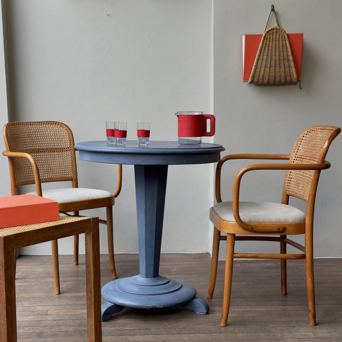Round blue painted pedestal table with two cane chairs and a red pitcher.