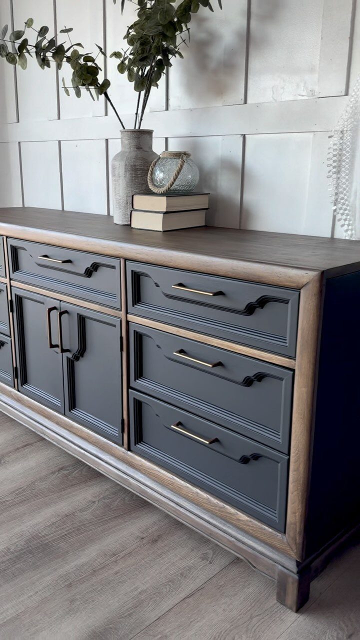 Dark blue painted sideboard with grey top and gold handles against white wall.