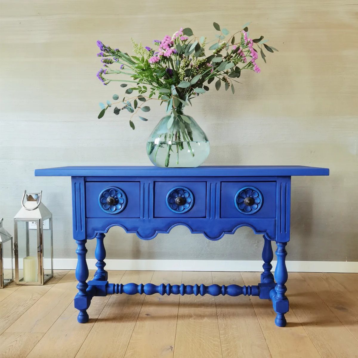 Medium blue painted console table with flowers in a glass vase on top.