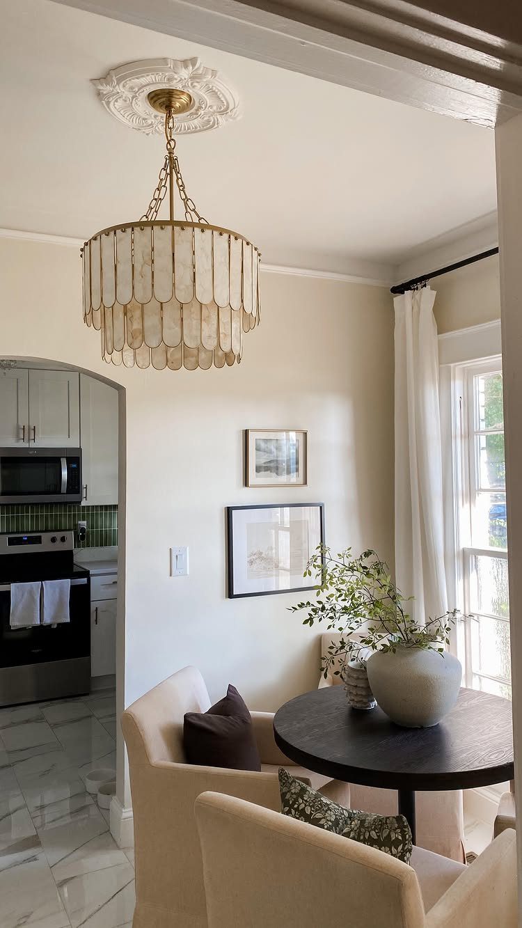 Small dining nook with round dark table, beige armchairs, and ornate chandelier.