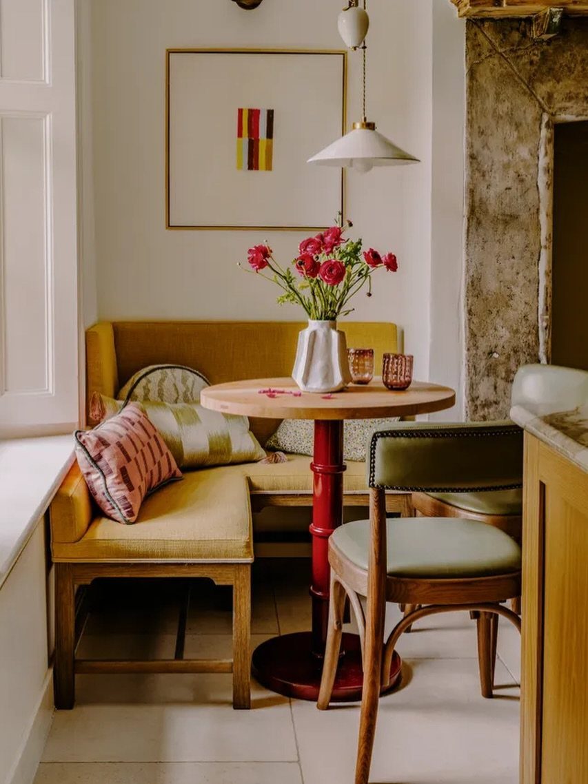 Yellow banquette and green chair surrounding a round wooden table with red flowers.