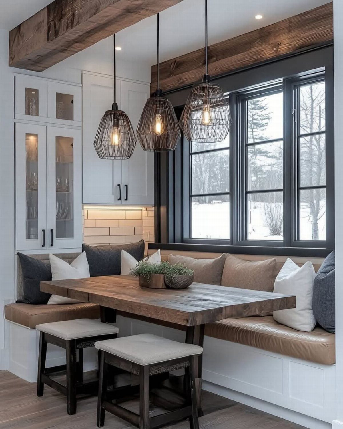 Wooden table and leather banquette seating under black wire pendant lights by a window