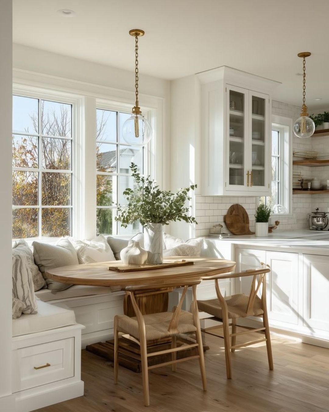 Modern farmhouse breakfast nook with white built-in seating, oval wooden table, and wishbone chairs.