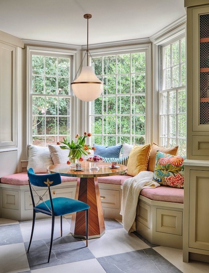 Breakfast nook with round wooden table, built-in bench, and bay window lighting.