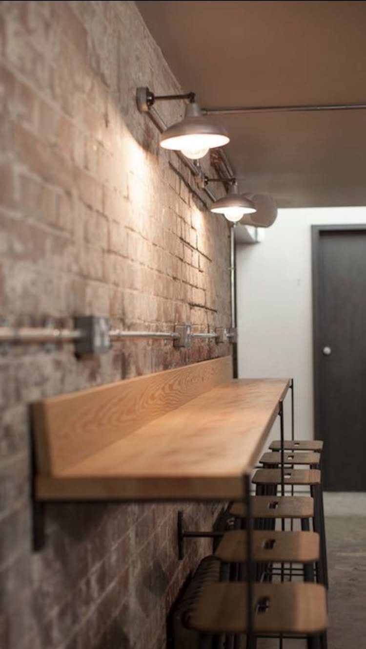Wooden wall-mounted counter and stools against a brick wall with industrial lighting.