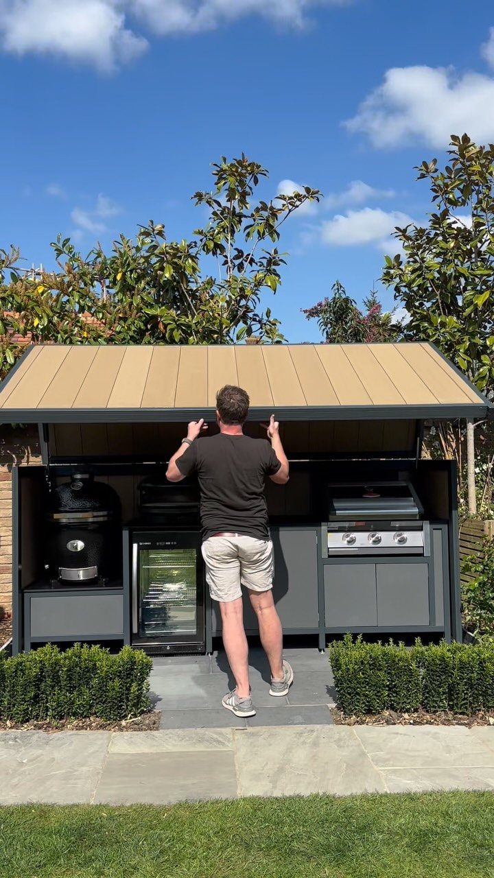 Covered outdoor kitchen station with built-in grill and refrigerator in a backyard setting.