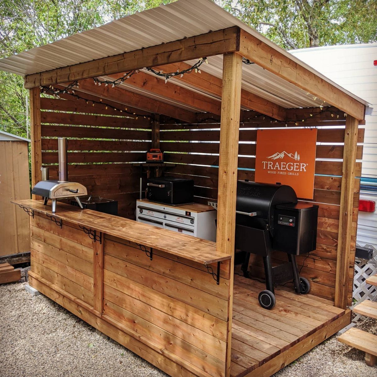 Wooden grill shed with a metal roof housing a black grill and counter.