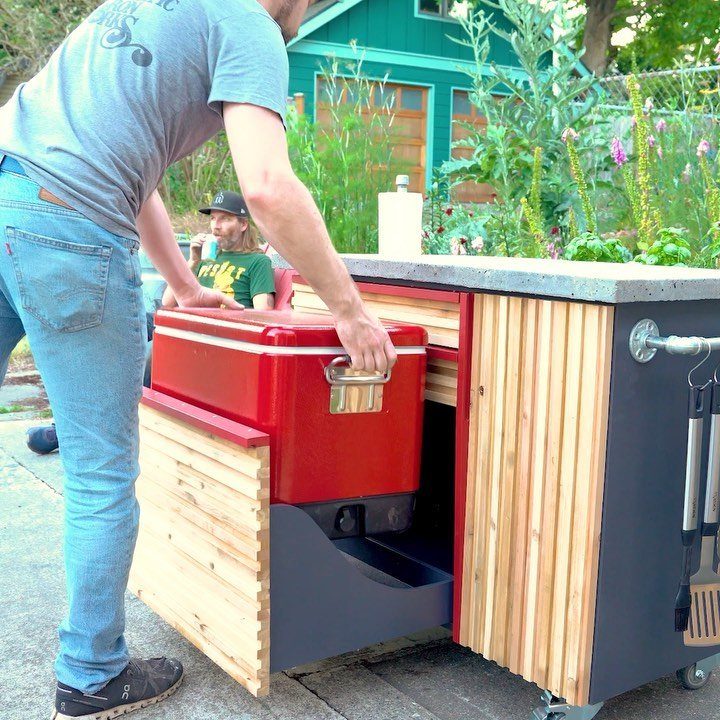 Man pulling a red cooler from a custom wooden outdoor grill station.