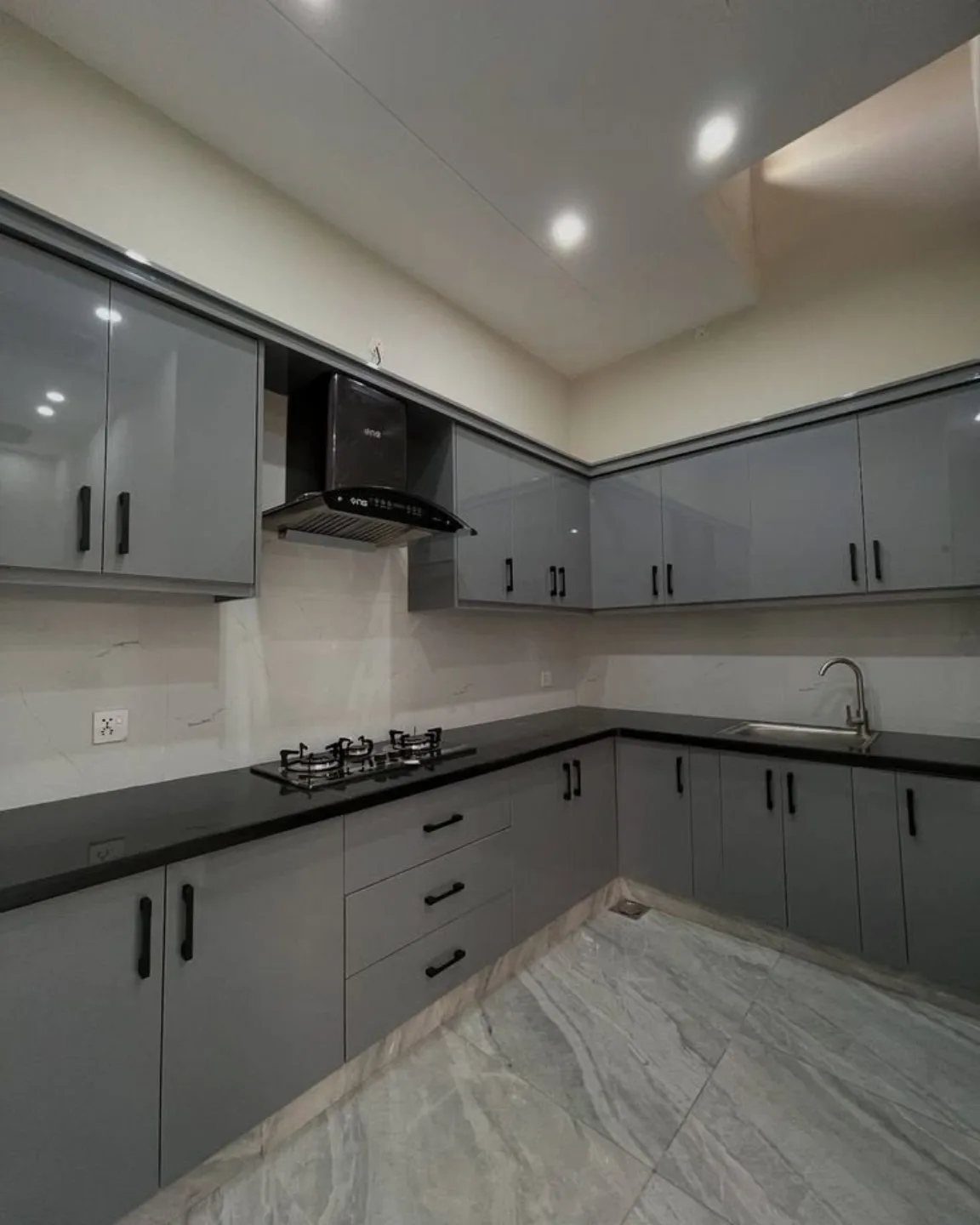 Light gray glossy kitchen cabinets with black countertops and white marble floors.