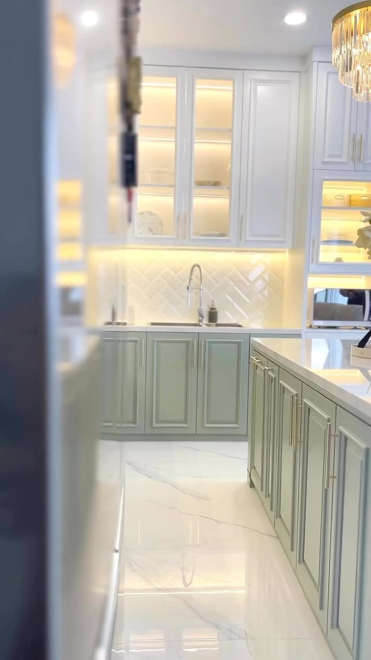 Sage green lower kitchen cabinets with white upper cabinets and white marble flooring.
