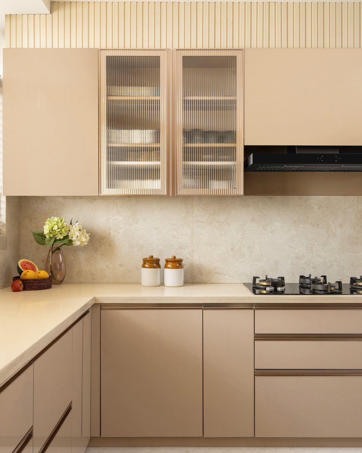 Beige flat-panel kitchen cabinets with fluted glass doors and light stone countertops.