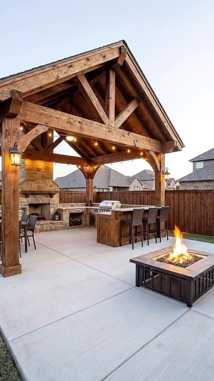 Wooden pavilion covering an outdoor kitchen and fireplace on a concrete patio