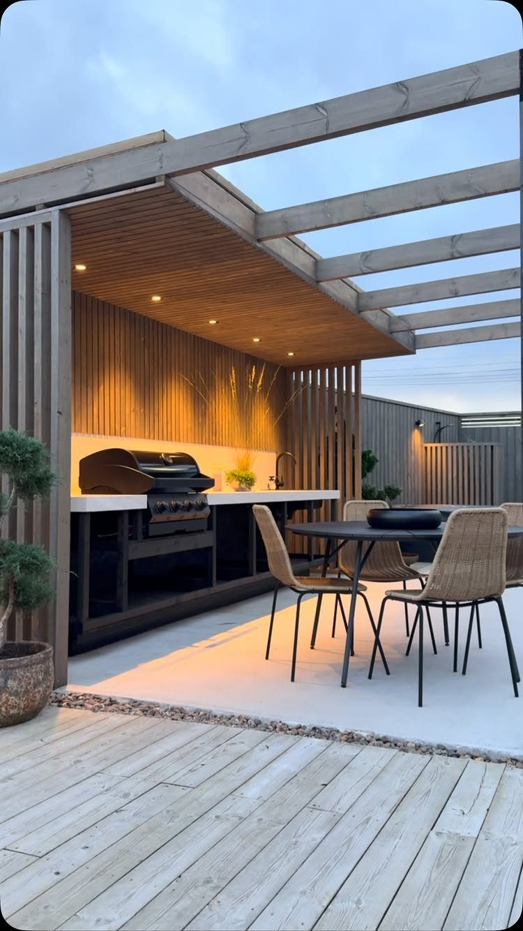 Modern outdoor kitchen with a wooden pergola, built-in grill, and dining set.