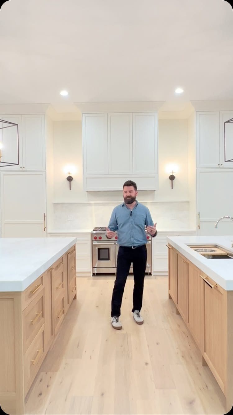 Man standing between two large white kitchen islands with light wood cabinetry.