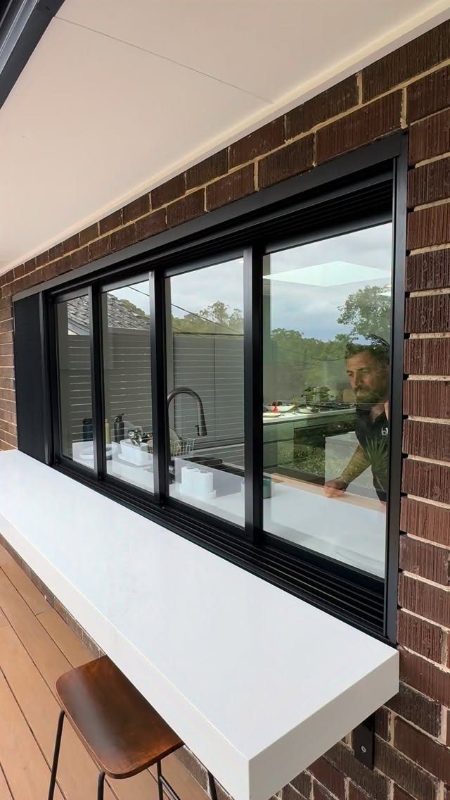 Large black-framed sliding glass window connecting a modern kitchen to an outdoor deck.