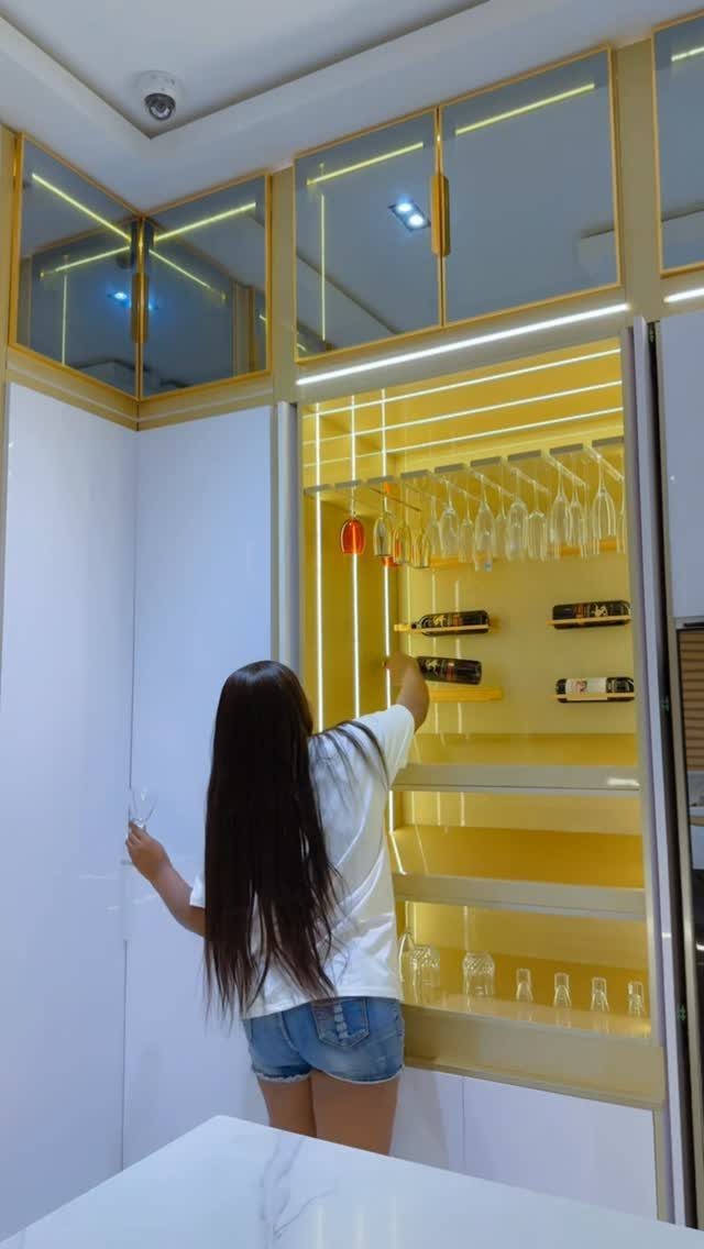 Woman reaching into a yellow kitchen cabinet with integrated LED strip lighting and glassware.