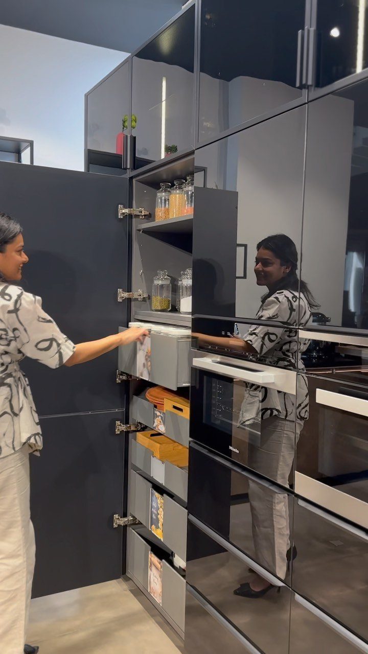 Woman opening a tall dark grey kitchen cabinet with organized pull-out storage drawers.