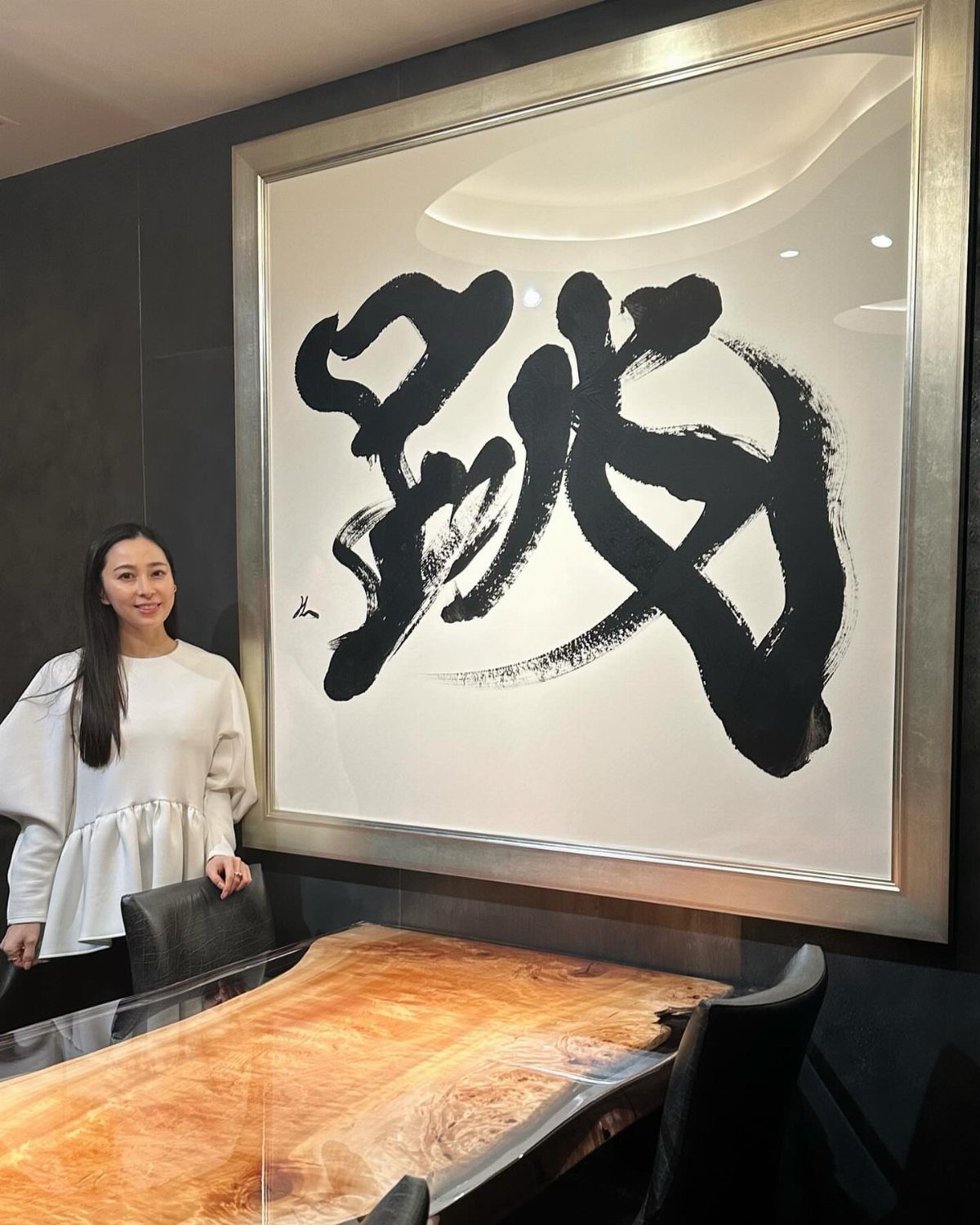 Large framed Japanese calligraphy art hanging on a dark wall above a wooden table.