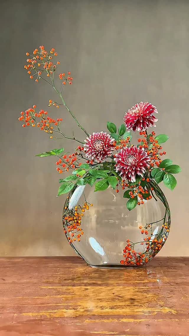 Ikebana flower arrangement with red chrysanthemums and orange berries in a glass vase.