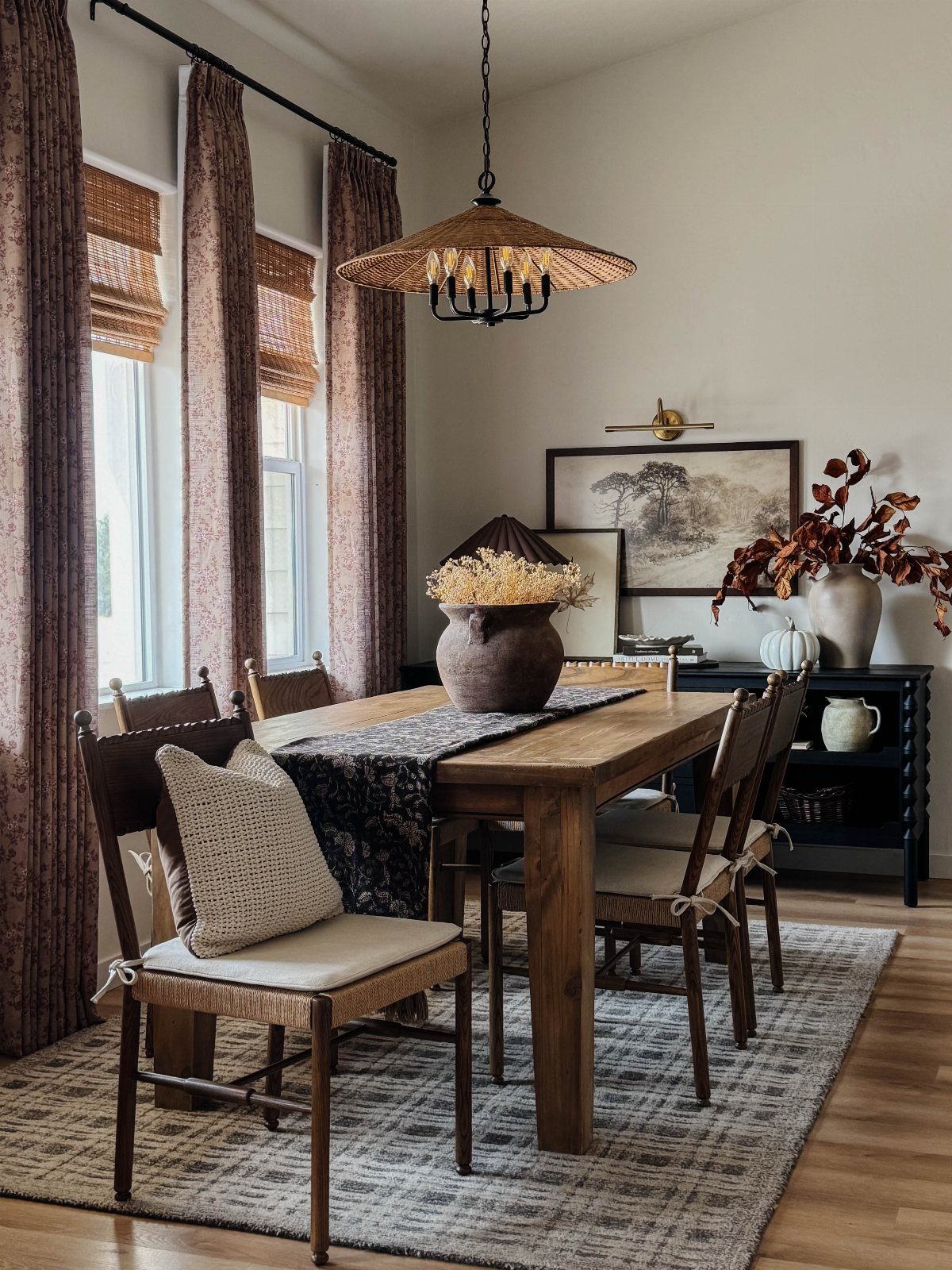 Wooden dining table and chairs in a room with woven lighting and curtains.