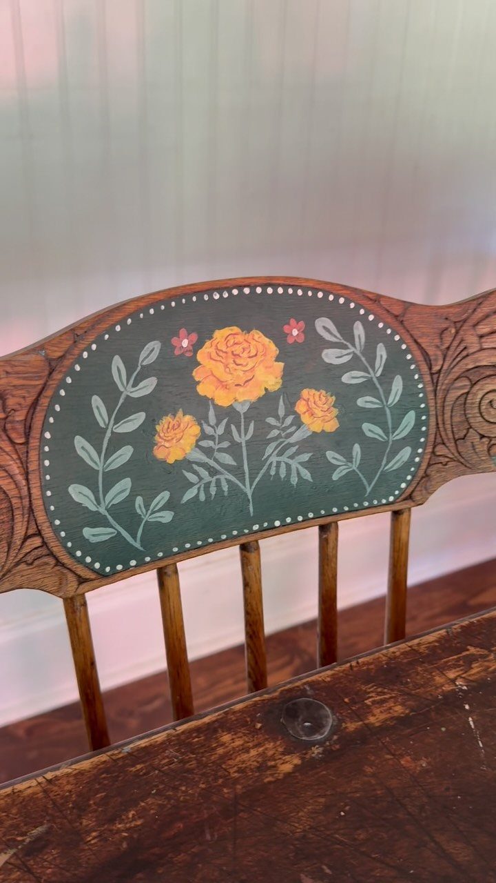 Wooden chair back with a painted green floral design and yellow flowers.