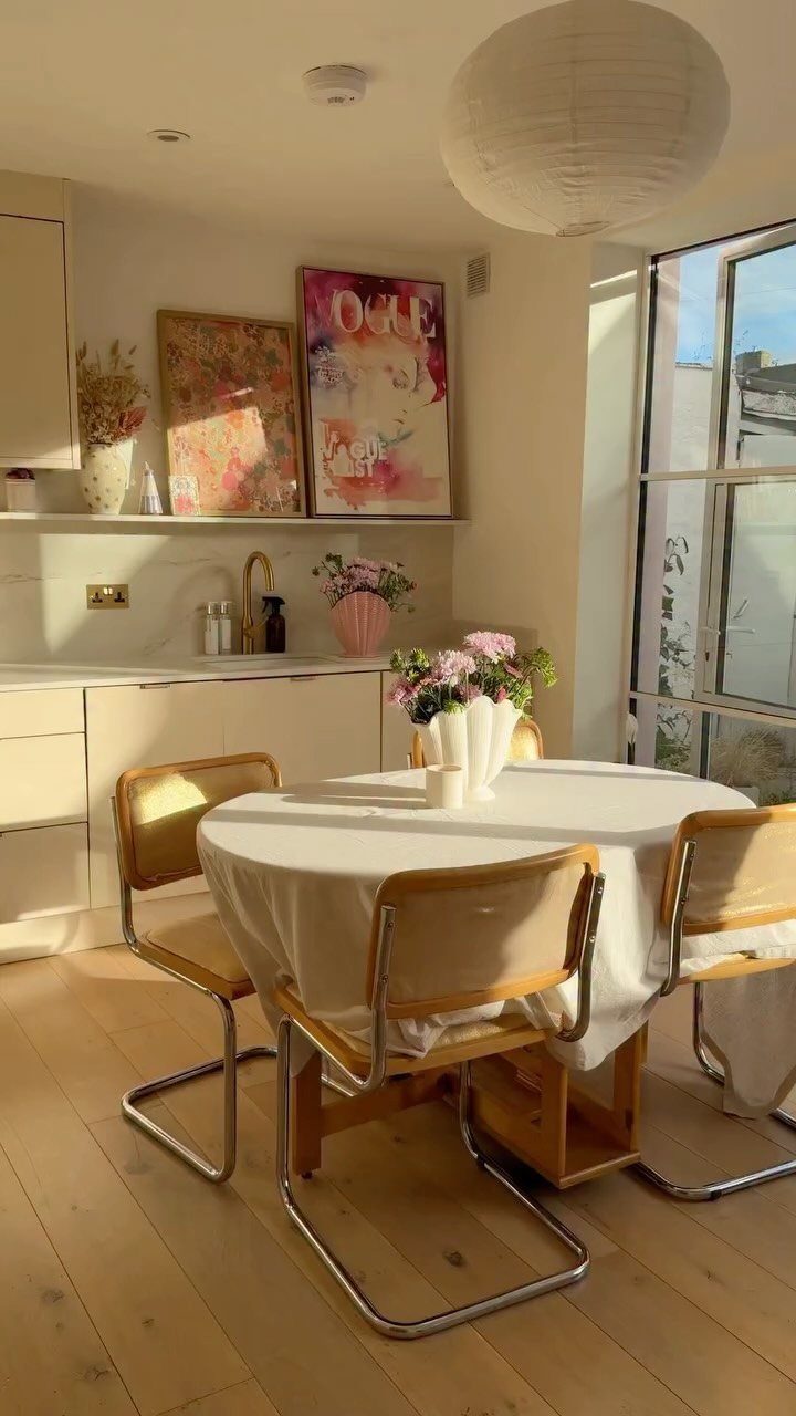 Round dining table with white tablecloth and pink flowers in a bright room.