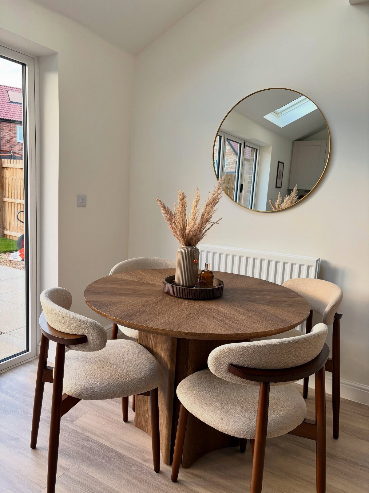 Round wooden dining table with cream chairs and a minimalist pampas grass centerpiece.