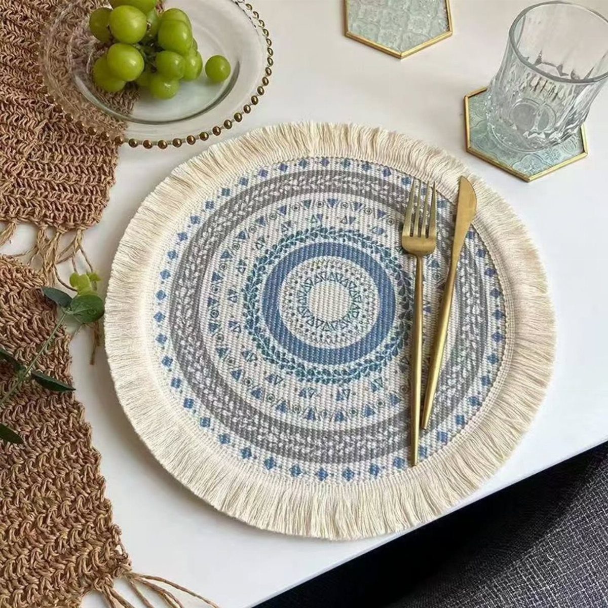Round woven placemat with blue patterns and gold cutlery on a white table.