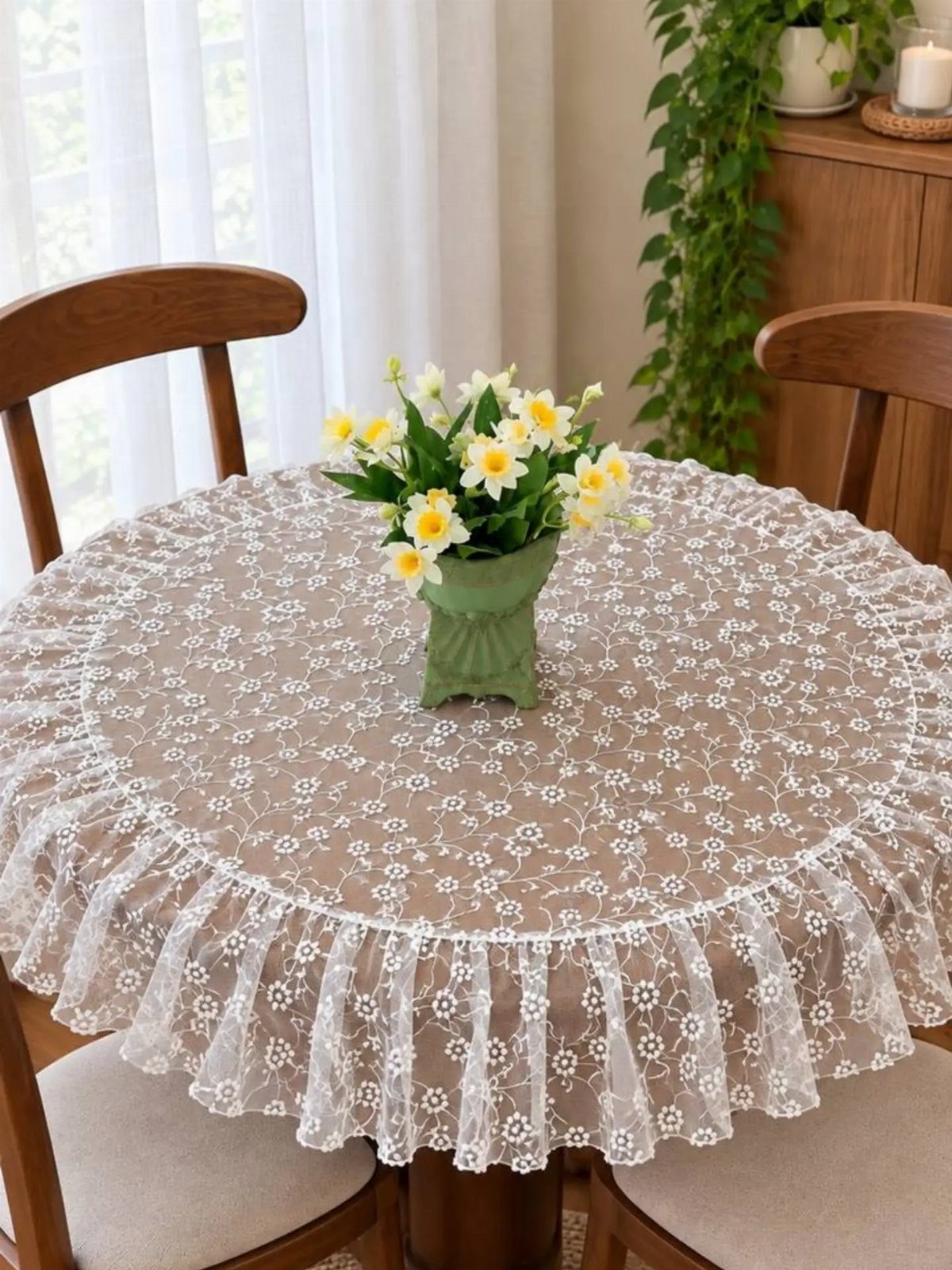 Round dining table covered in a white lace tablecloth with yellow flowers centerpiece.