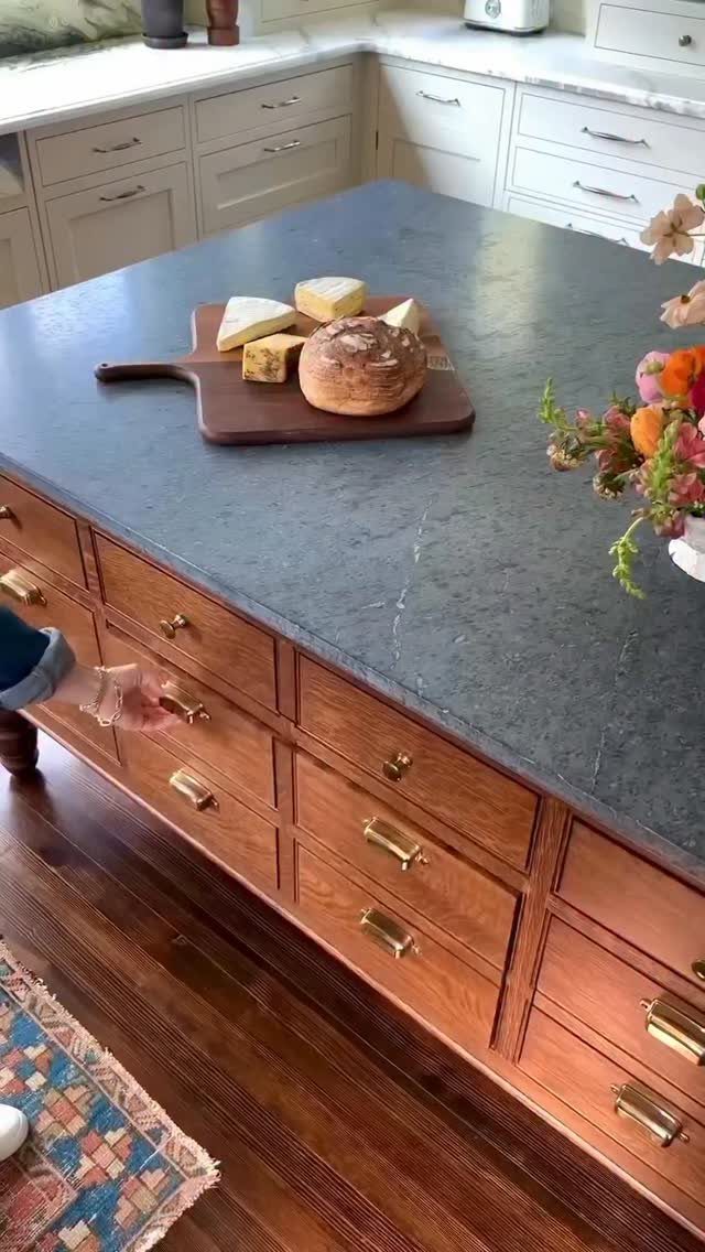 Wooden kitchen island with dark grey stone countertop and a cheese board.