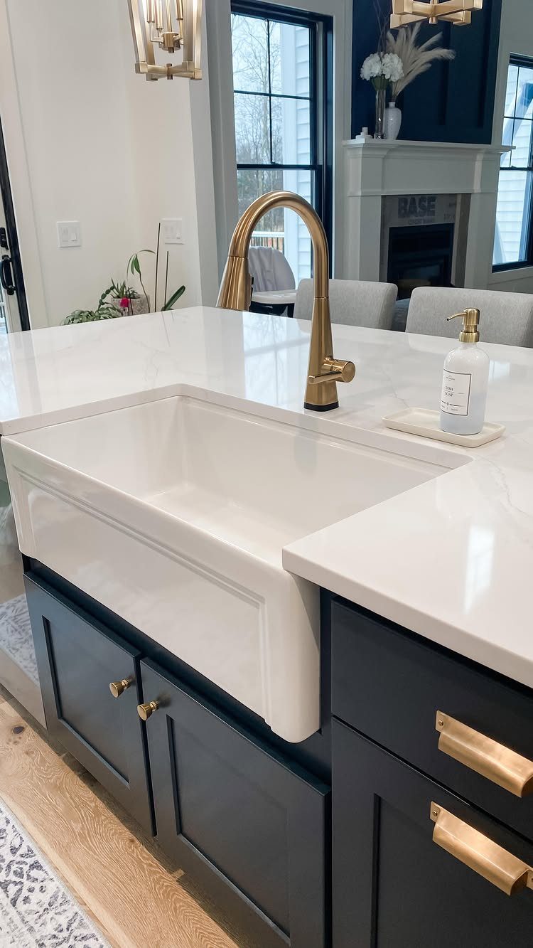 White farmhouse sink with gold faucet installed in navy blue kitchen cabinetry