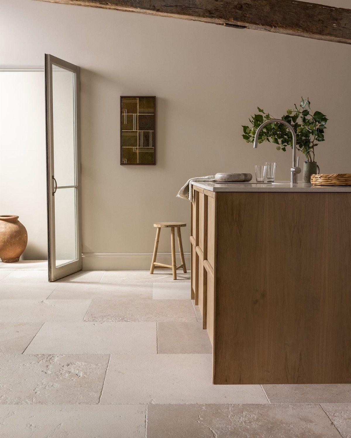 Weathered stone floor tiles in a kitchen with a wooden island and beam.