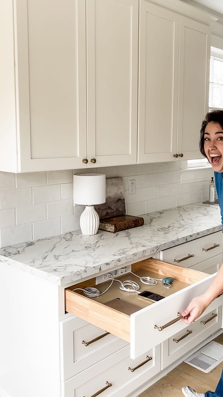 Woman opening a white kitchen drawer containing built-in power outlets and charging cables.
