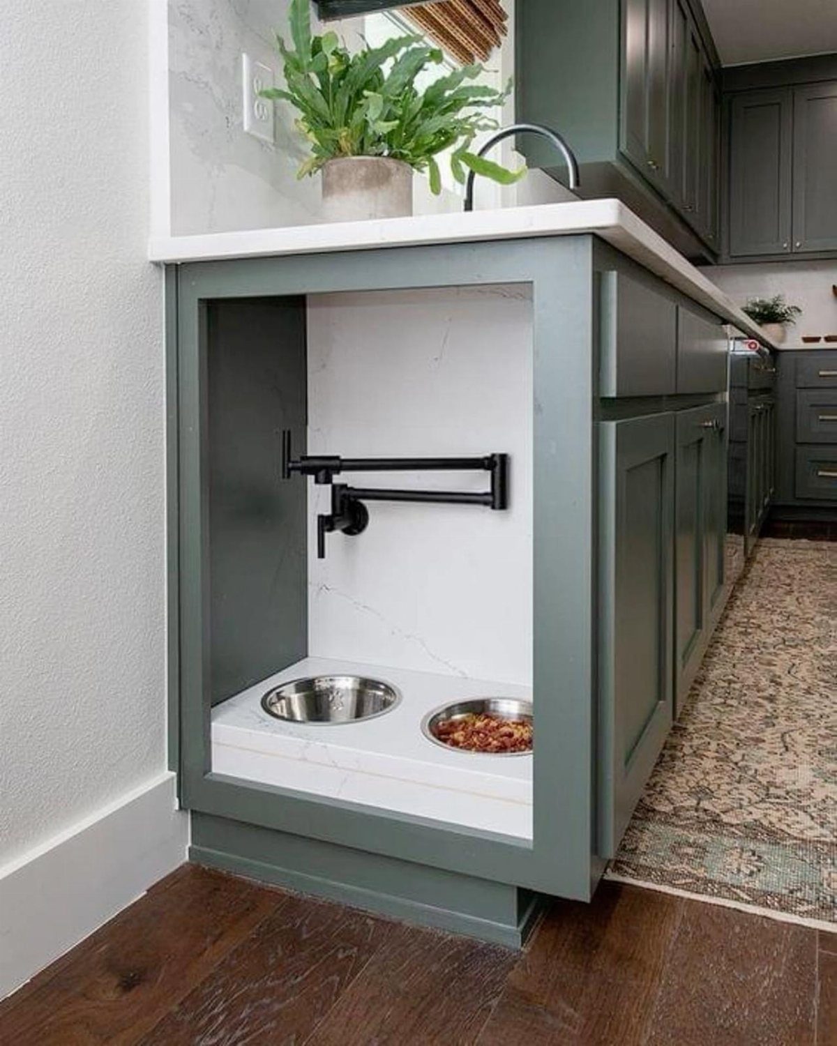Built-in pet feeding station with stainless steel bowls in a green kitchen island.