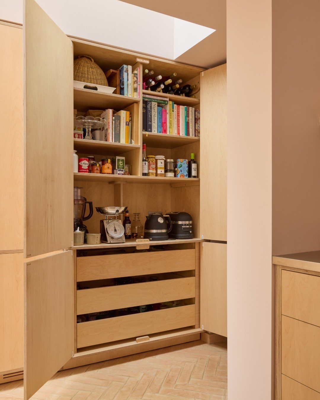 Light wood kitchen pantry with open doors revealing shelves and pull-out drawers.