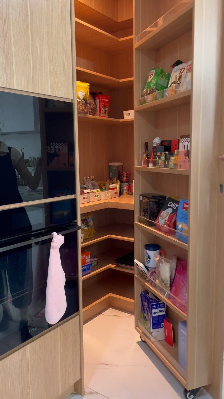 Pull-out pantry cabinet with light wood shelves holding various dry food packages.