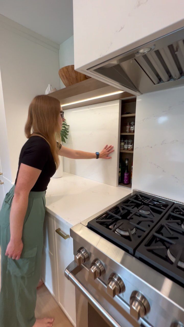 Woman pulling out a narrow vertical spice rack next to a kitchen stove.
