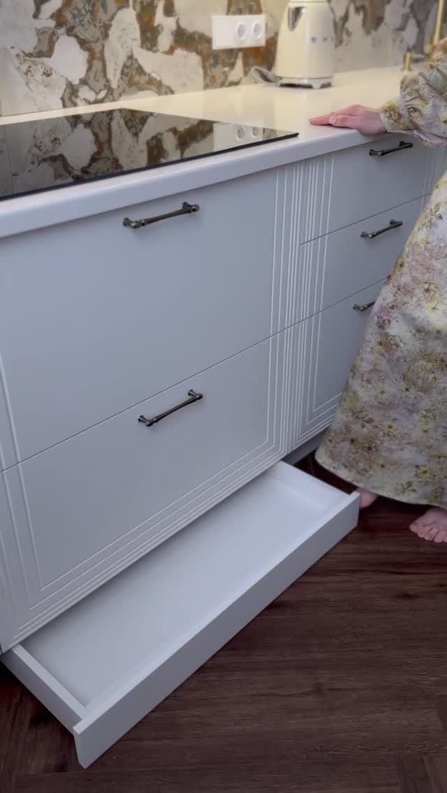 White kitchen cabinet with a shallow toe-kick drawer open at the base.