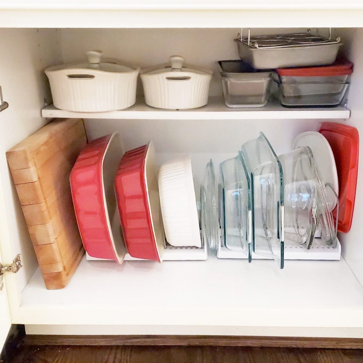 Baking pans and glass dishes stored vertically in a white kitchen cabinet organizer.