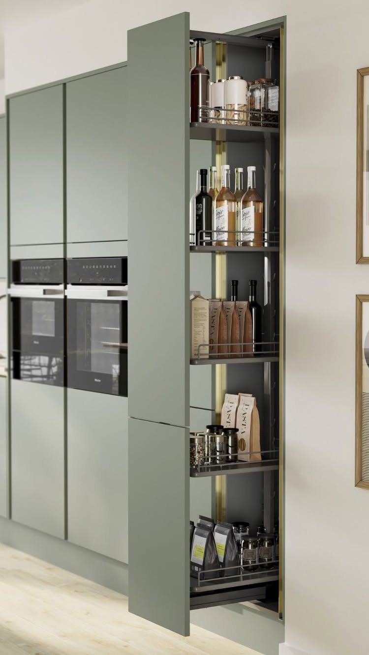 Pull-out sage green pantry cabinet filled with bottles and jars in a modern kitchen.