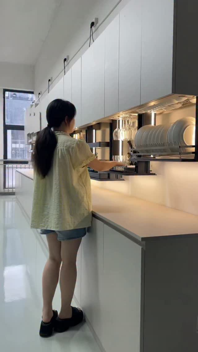Woman using a pull-down dish rack in a kitchen with white minimalist cabinetry.